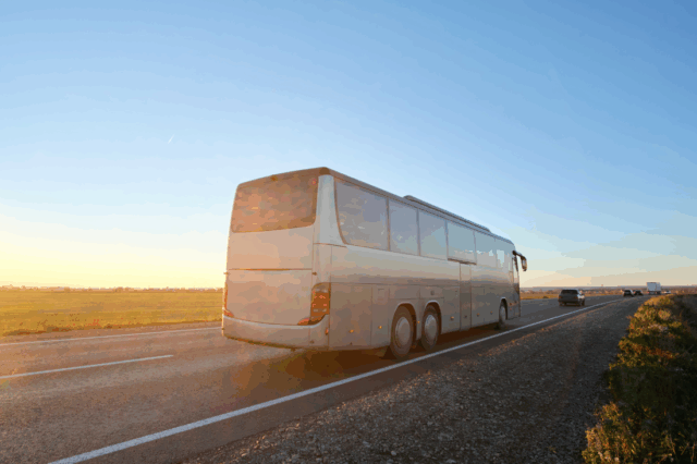 A large bus driving on a highway at sunset.