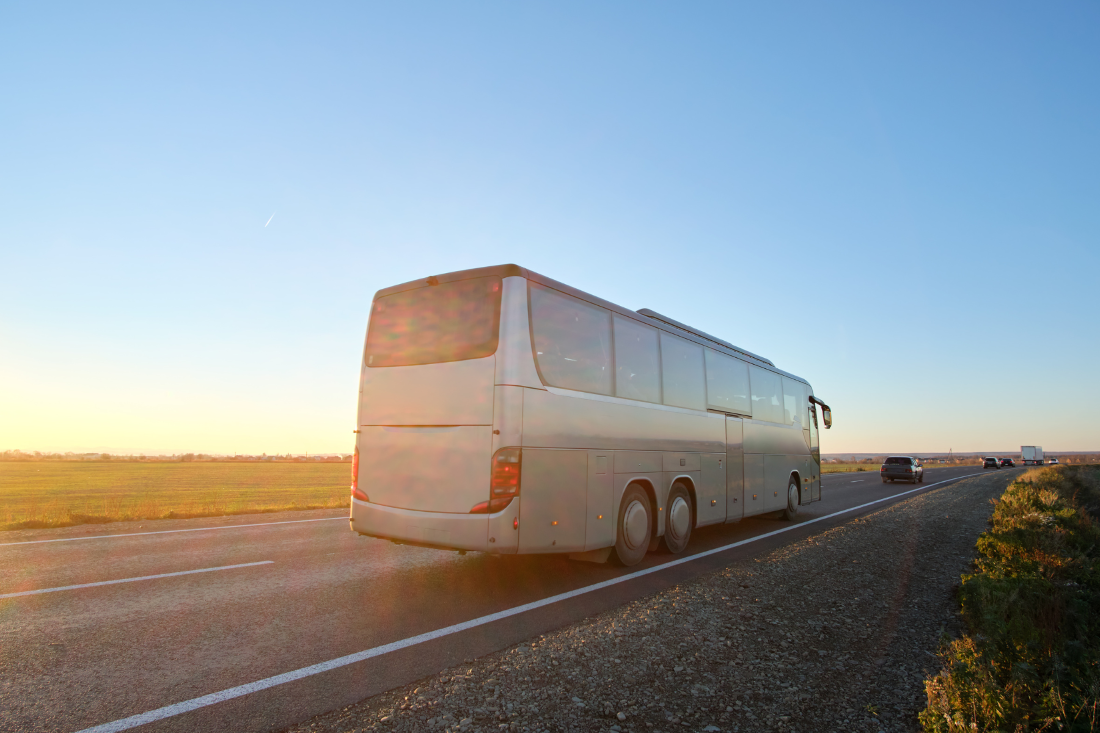A large bus driving on a highway at sunset.
